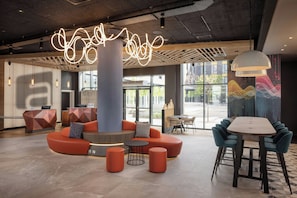 Un vestíbulo moderno con una zona de estar central, una recepción y un comedor con sillas y mesas.