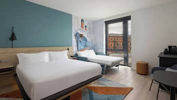Ein Hotelzimmer mit zwei Betten, einem Schreibtisch, einem Stuhl, einer Lampe und einem großen Fenster mit Blick auf Gebäude.