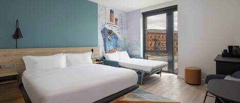 A hotel room with two beds, a desk, a chair, a lamp, and a large window with a view of buildings.