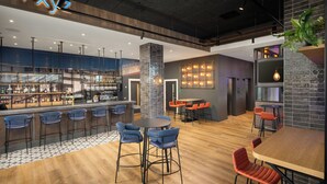 Un área de bar moderna con barra, taburetes y zona de estar con mesas y sillas.