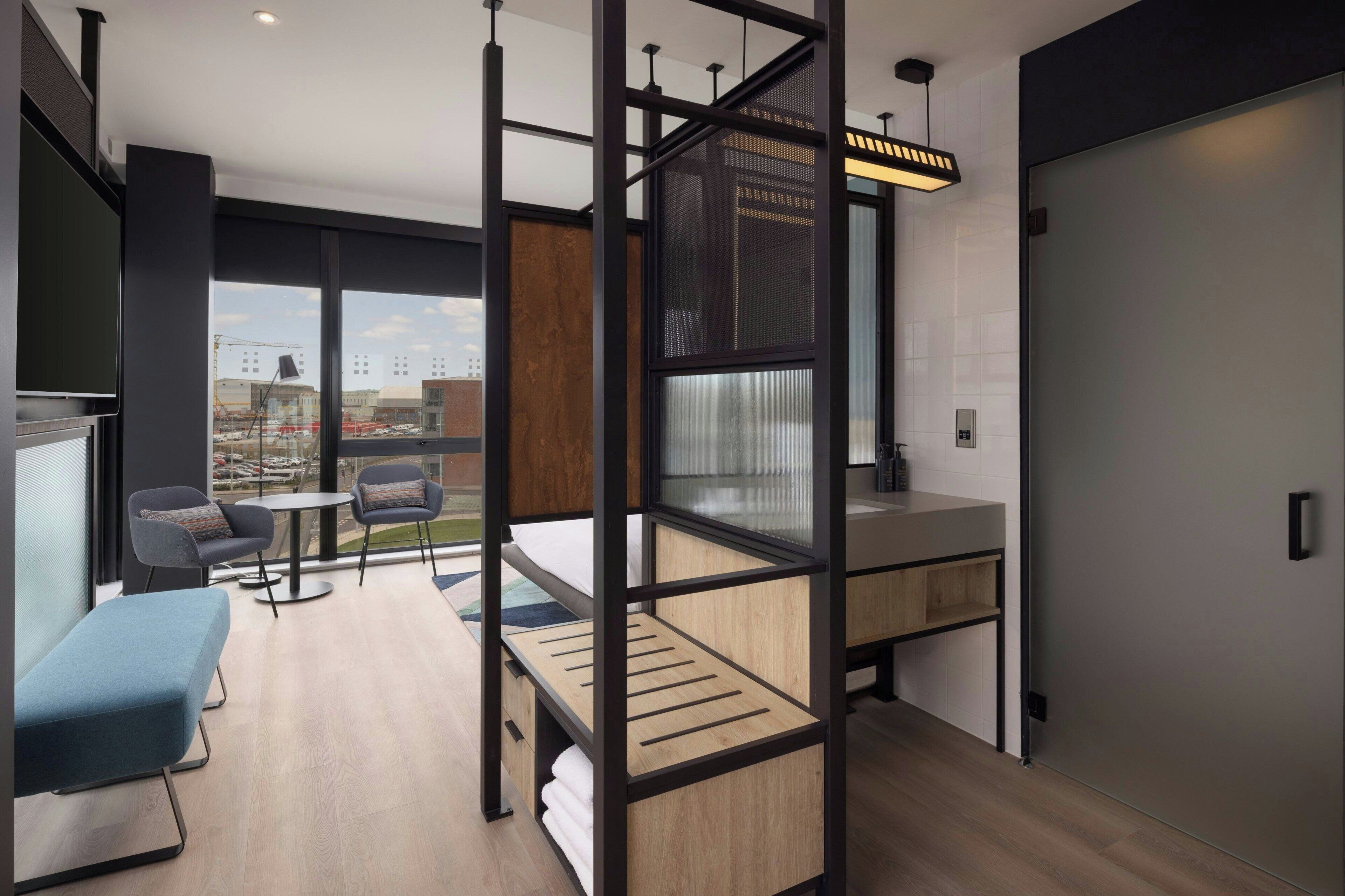 Habitació d'hotel moderna amb una finestra gran, un balcó, una taula de treball i una zona d'estar.