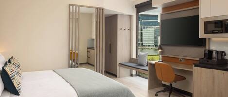 Une chambre d’hôtel moderne équipée d’un lit, d’un bureau, d’une chaise et d’une grande fenêtre donnant sur la ville.