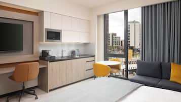 A modern hotel room with a kitchenette, a large bed, a sofa, and a dining area.