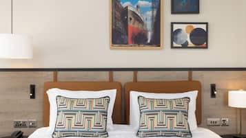 A hotel room with a bed, two patterned pillows, a nightstand, a phone, a lamp, and three framed artworks on the wall.