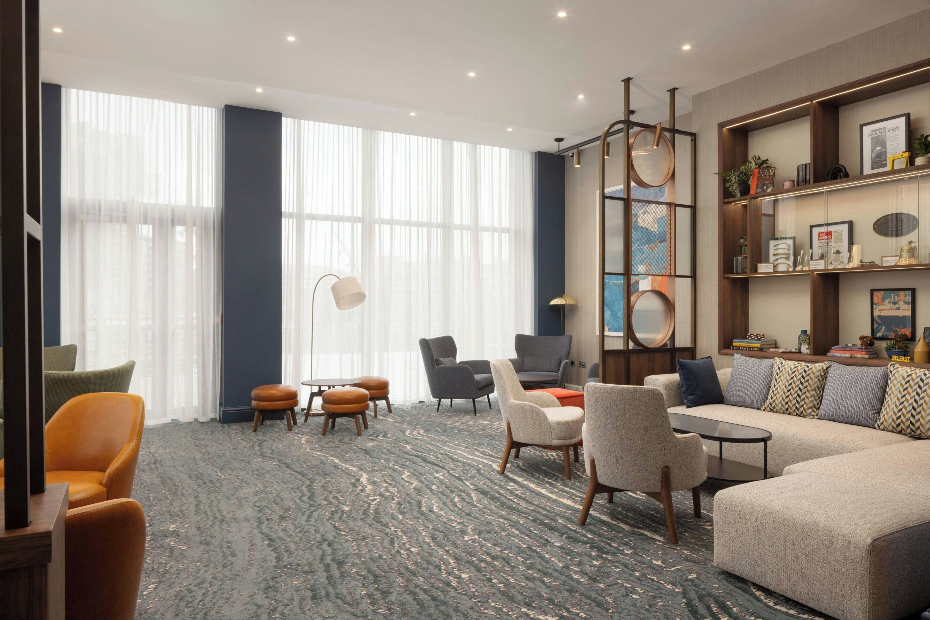 A modern hotel lobby with a large window, seating area, and a bookshelf.