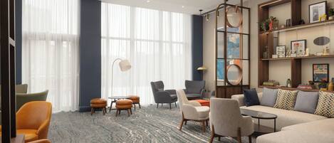 A modern hotel lobby with a large window, seating area, and a bookshelf.