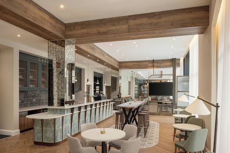 A modern kitchen with a bar area, wooden beams, and a dining space with round tables and chairs.. Residence Inn By Marriott Belfast Titanic Quarter