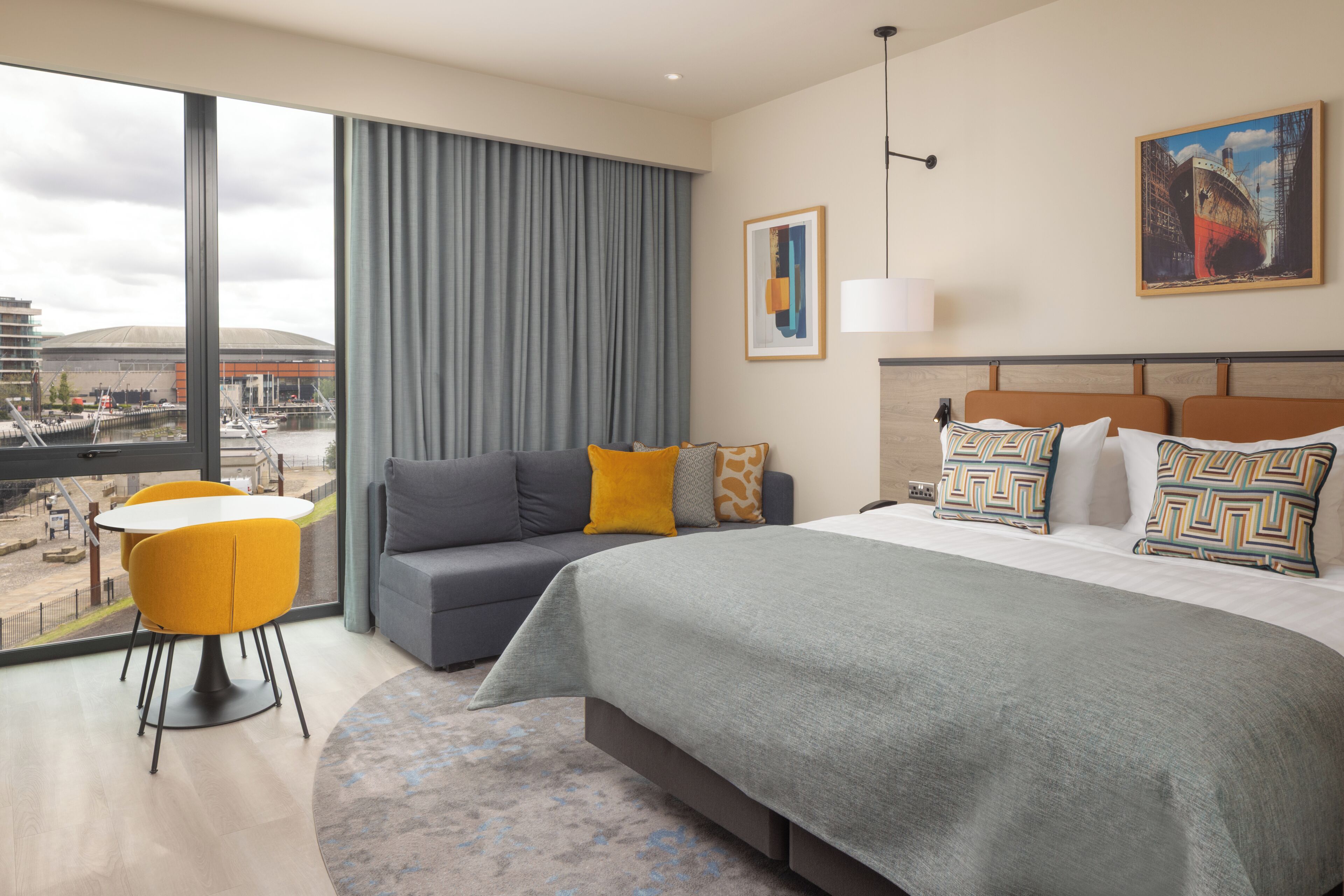 Une chambre d’hôtel avec un grand lit, un canapé, une table à manger et une vue sur un port.
