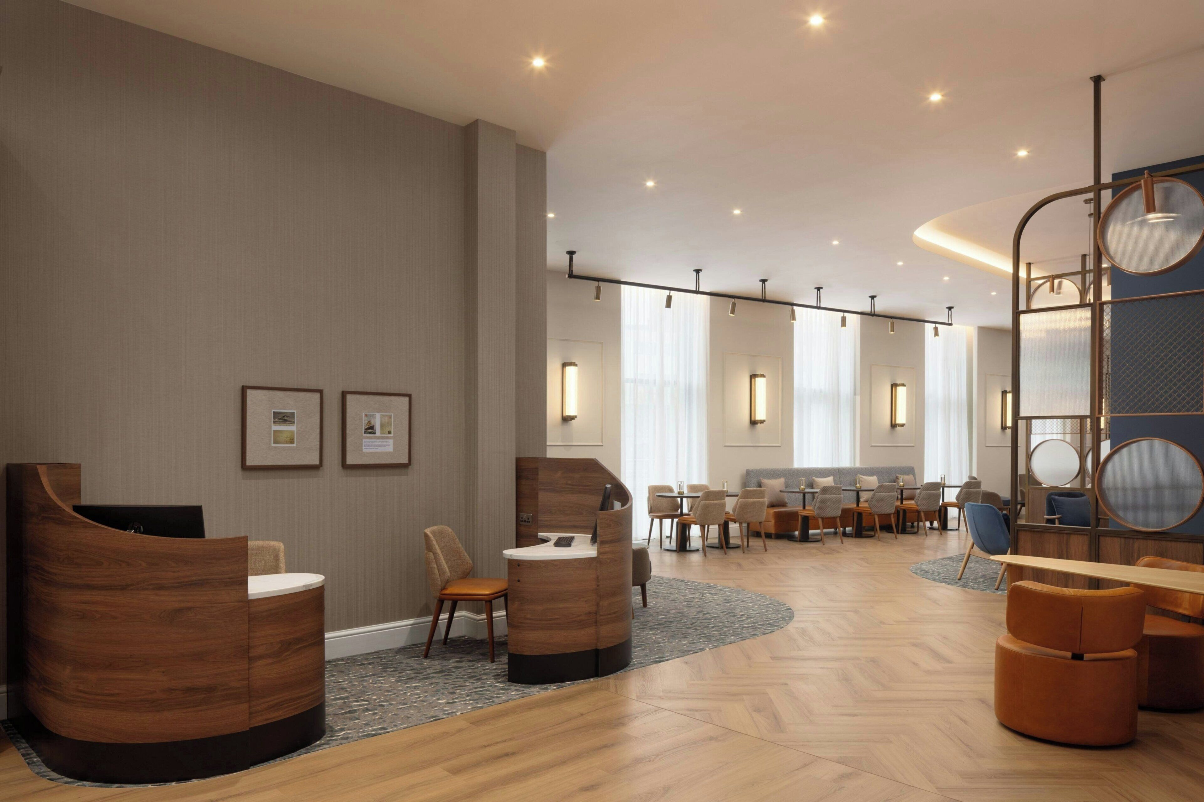 A modern hotel lobby with a reception desk, seating area, and a large mirror.