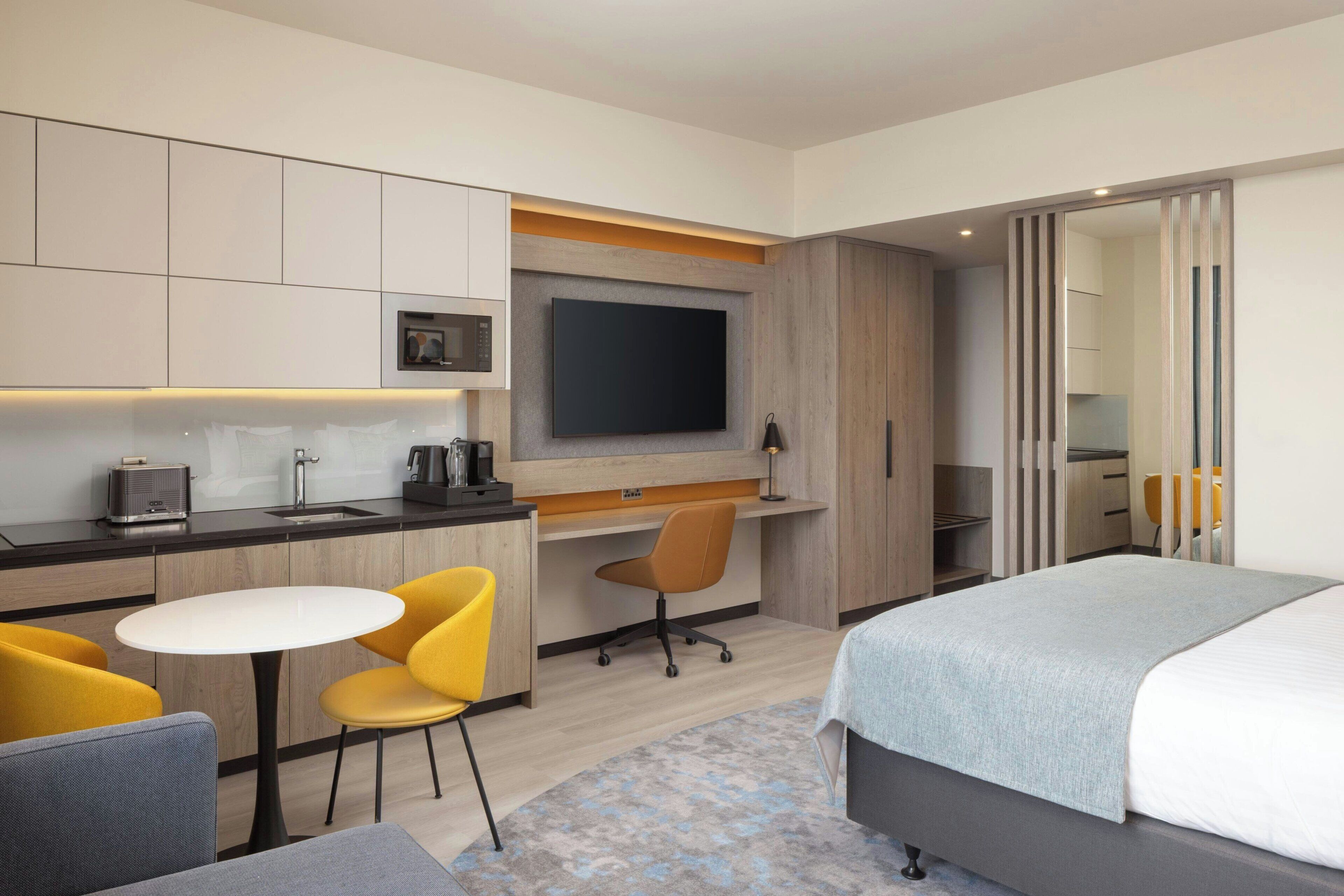 Une chambre d’hôtel comprenant un lit, un bureau avec une chaise, une télévision et une kitchenette.