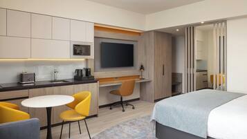 Une chambre d’hôtel comprenant un lit, un bureau avec une chaise, une télévision et une kitchenette.
