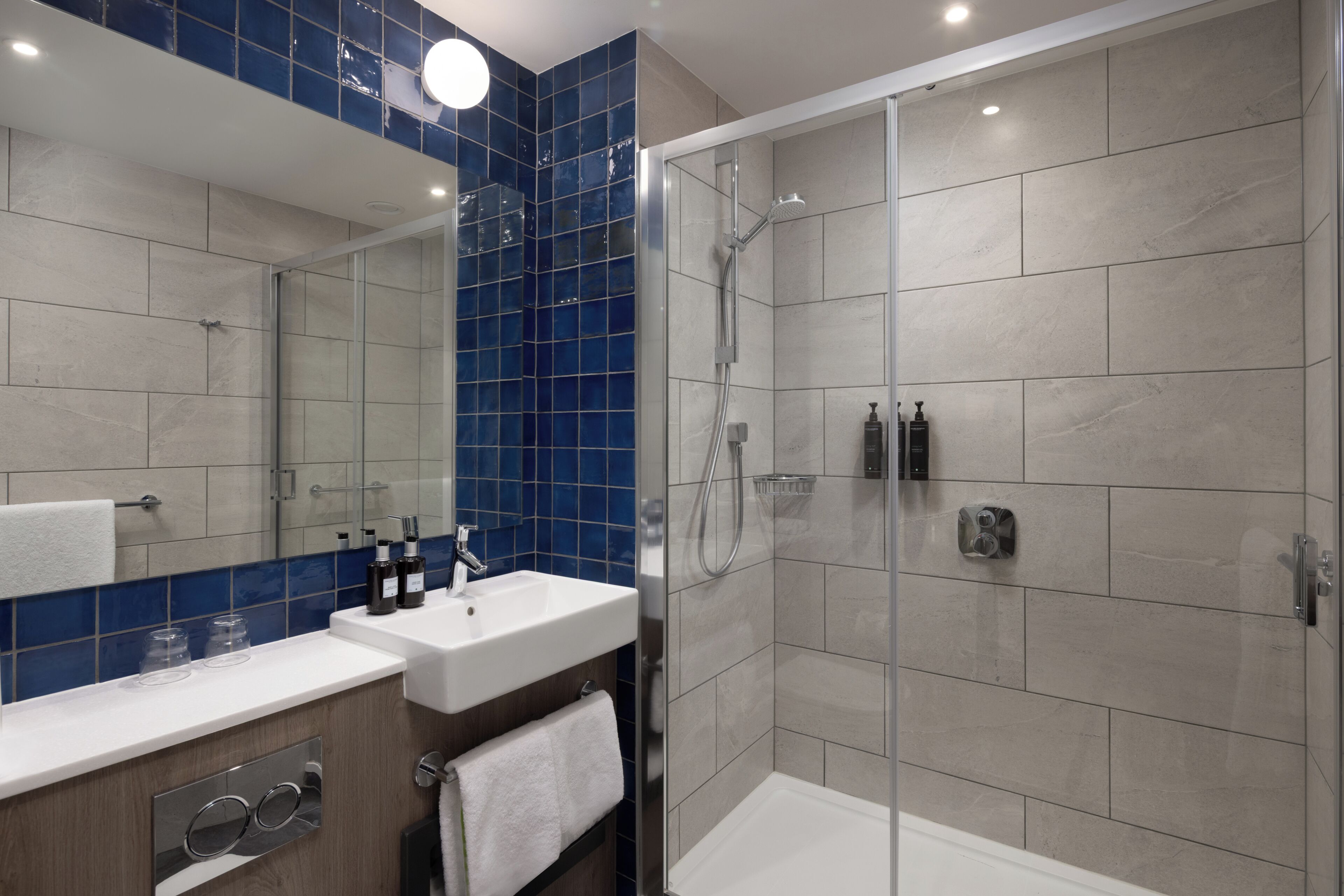 Een moderne badkamer met een douchecabine van glas, een witte wastafel en een spiegel boven het aanrecht.