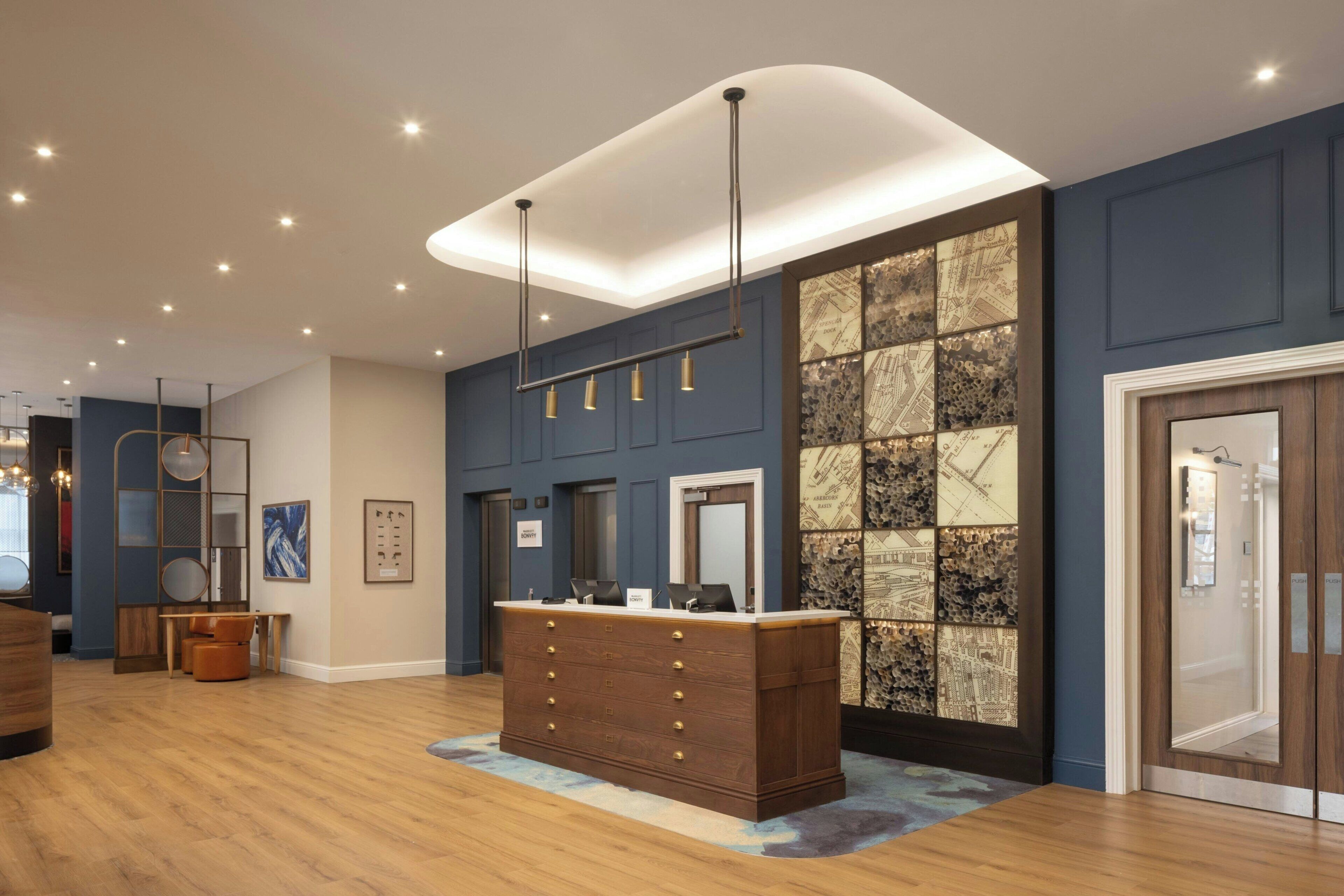 Un mostrador de recepción con detalles de madera, una lámpara colgante moderna y un mural con vista a la ciudad.