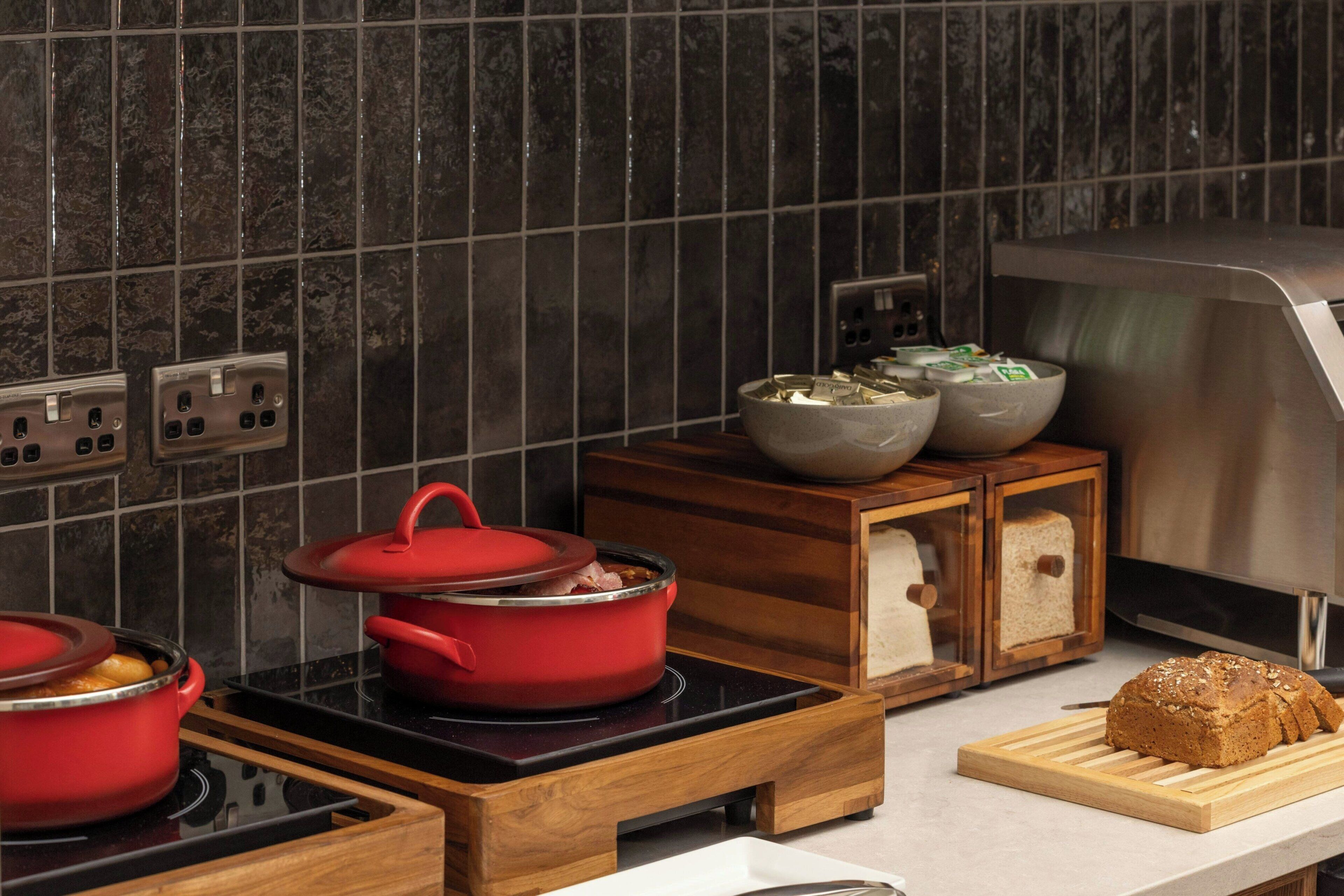 A kitchen with a red pot on an induction cooktop, a loaf of bread on a cutting board, and wooden cabinets with glass doors.
