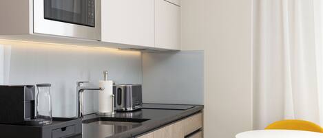 Cozinha moderna com micro-ondas embutido, cafeteira e torradeira. Há uma pequena área de jantar com uma mesa branca e cadeiras amarelas.