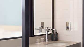 A modern bathroom with a large mirror, a chrome faucet, and two glass bottles on the sink.