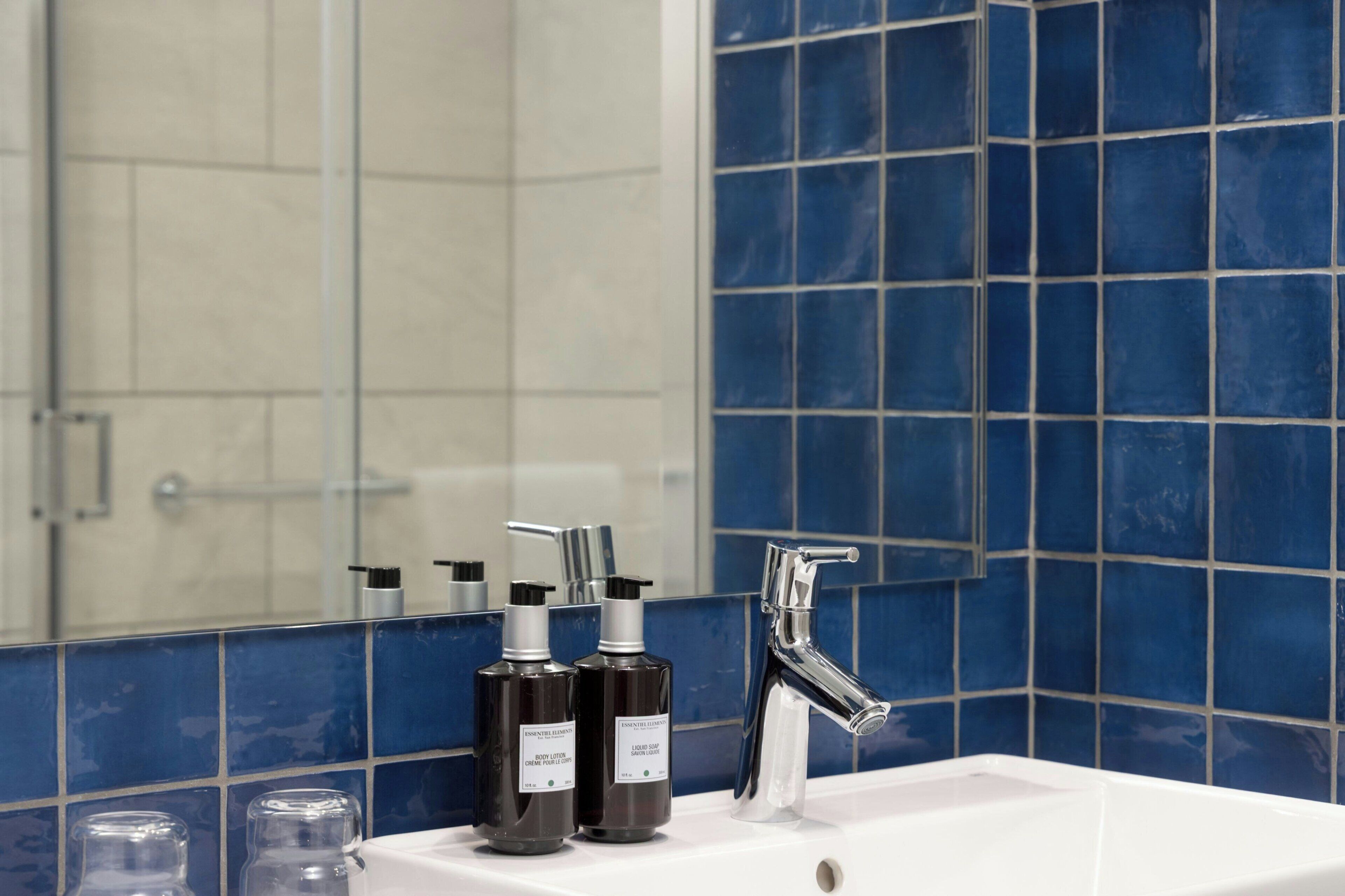 A bathroom with a white sink, two black bottles of liquid soap, a chrome faucet, and blue-tiled walls.