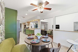 Une cuisine moderne avec un coin repas, un ventilateur de plafond et un téléviseur fixé au mur.