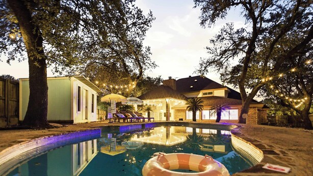 Una piscina con zona de descanso, una estructura de techo de paja y luces colgantes.