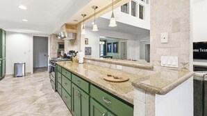 Una cocina moderna con armarios verdes, encimeras de granito e iluminación colgante.