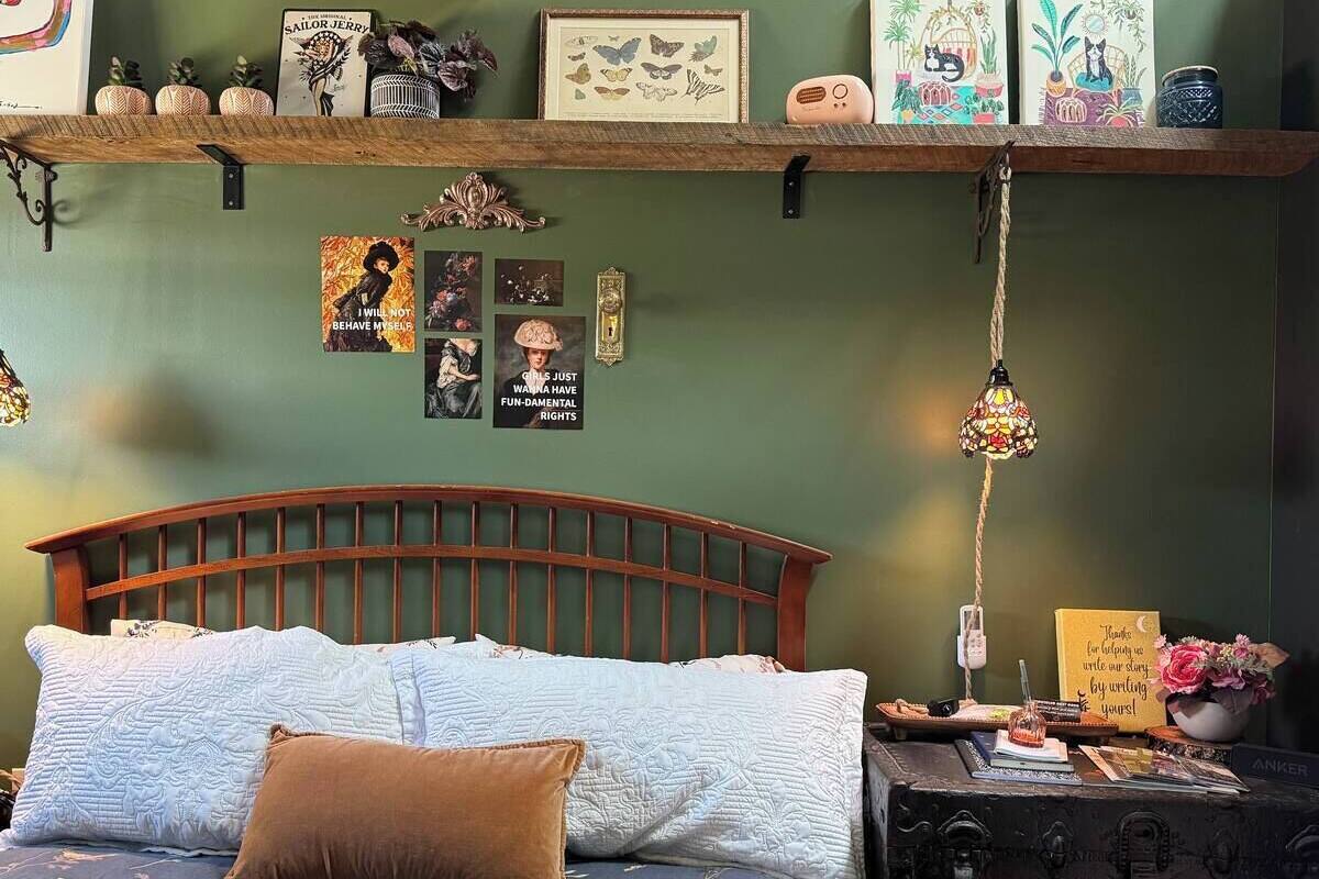 A bedroom with a wooden headboard, a bed with patterned bedding, a nightstand with a lamp, and wall decorations including framed pictures and a shelf with various items.