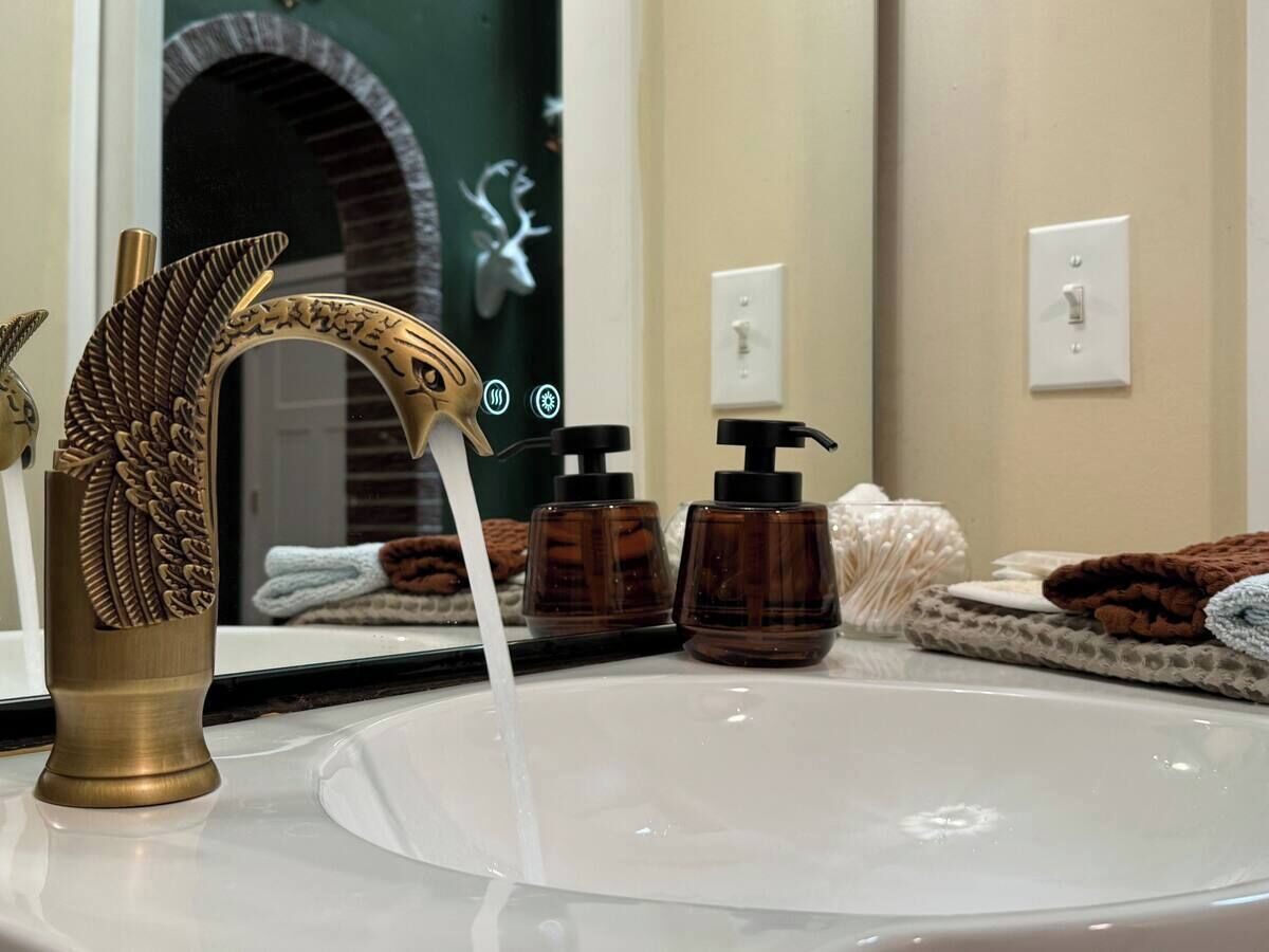 A bathroom with a brass faucet, soap dispensers, and towels.