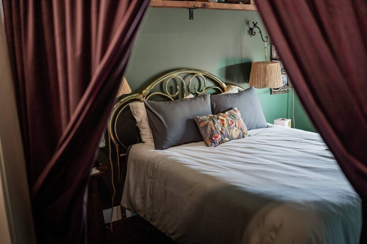 A bed with a metal headboard, grey bedding, and a floral pillow.