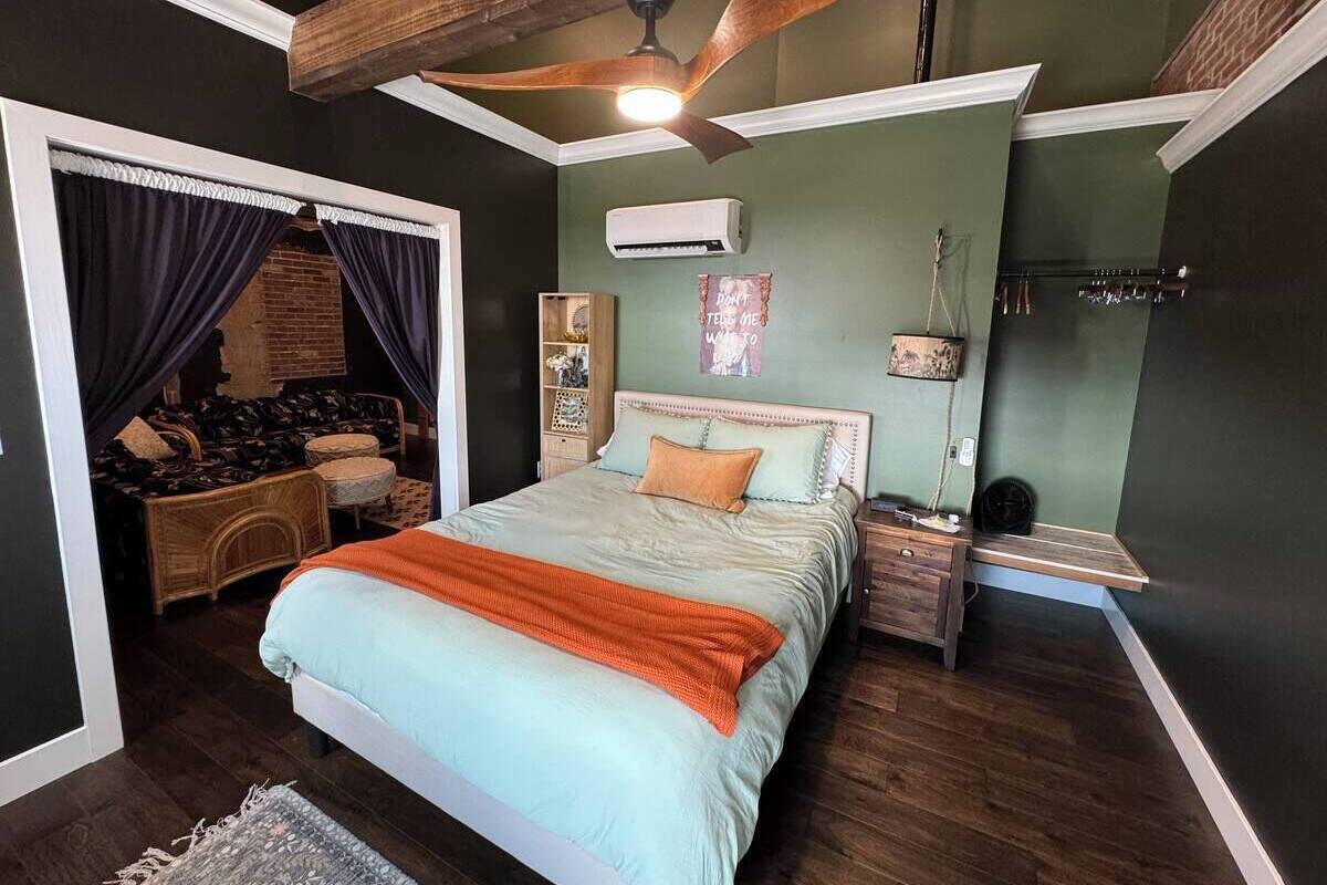 A bedroom with a bed, a nightstand, a dresser, a ceiling fan, and a window with curtains.