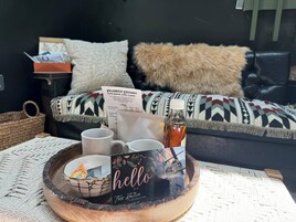 Un rincón acogedor con un revistero de madera que sostiene un menú, dos tazas, una botella y una tarjeta decorativa.