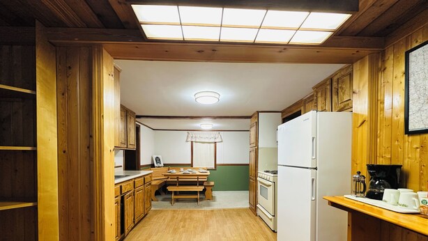 A kitchen with wooden cabinets, a white refrigerator, a stove, and a dining table with chairs. - Cozy bungalow in downtown Zelie remote-work ready (Zelienople)