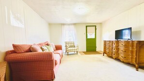 A living room with a red plaid sofa, a wooden dresser with a television, and a green door. - Cozy bungalow in downtown Zelie remote-work ready (Zelienople)