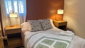 A bedroom with a bed, two bedside tables with lamps, a nightstand, a window with curtains, and a door. - Cozy bungalow in downtown Zelie remote-work ready (Zelienople)