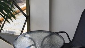 Un tavolo rotondo con piano in vetro lavorato, posizionato vicino a una finestra che si affaccia su un pavimento piastrellato e una pianta all'esterno.