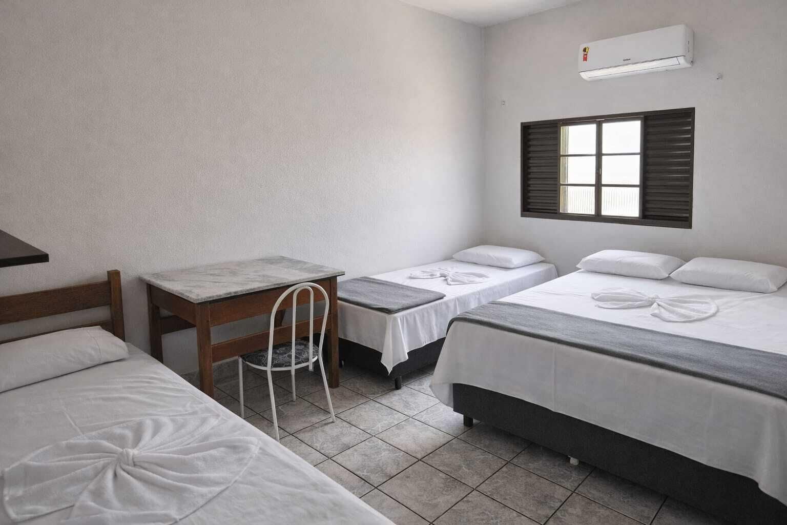 A hotel room with two beds, a desk, a chair, and an air conditioning unit.