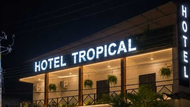 Un hotel chiamato 'HOTEL TROPICAL' dal design moderno, con un balcone adornato da piante e una targa che indica 'PAPELHINIA'.
