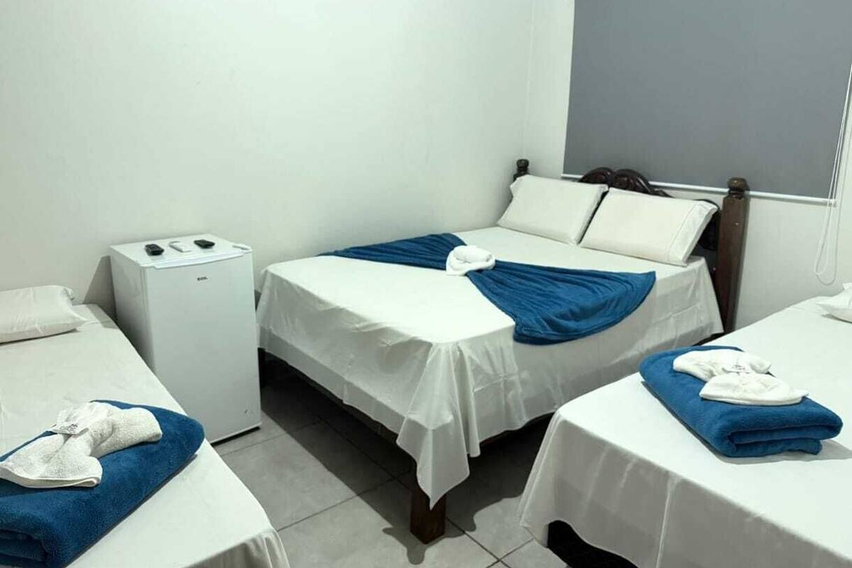A hotel room with two beds, a small white heater, and a window with a view.