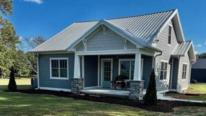 A single-story house with a gabled roof, a front porch with a bench, and stone pillars.
