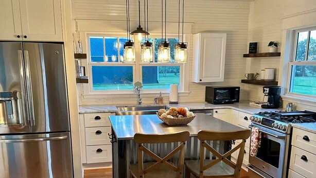 A modern kitchen with wooden flooring, stainless steel appliances, and a central island with chairs.