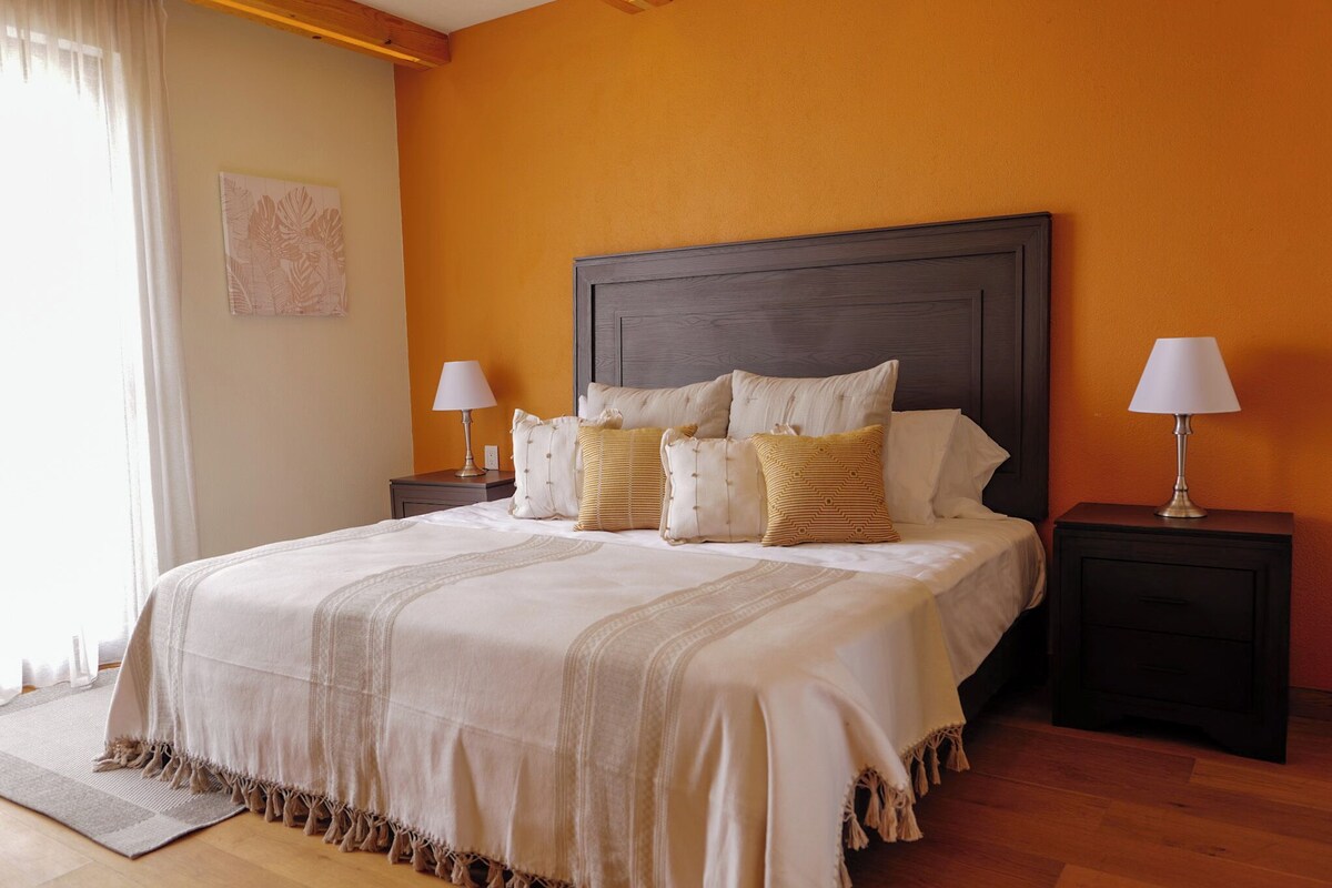 A neatly made bed with a dark headboard, two bedside tables with lamps, and a large window with curtains.