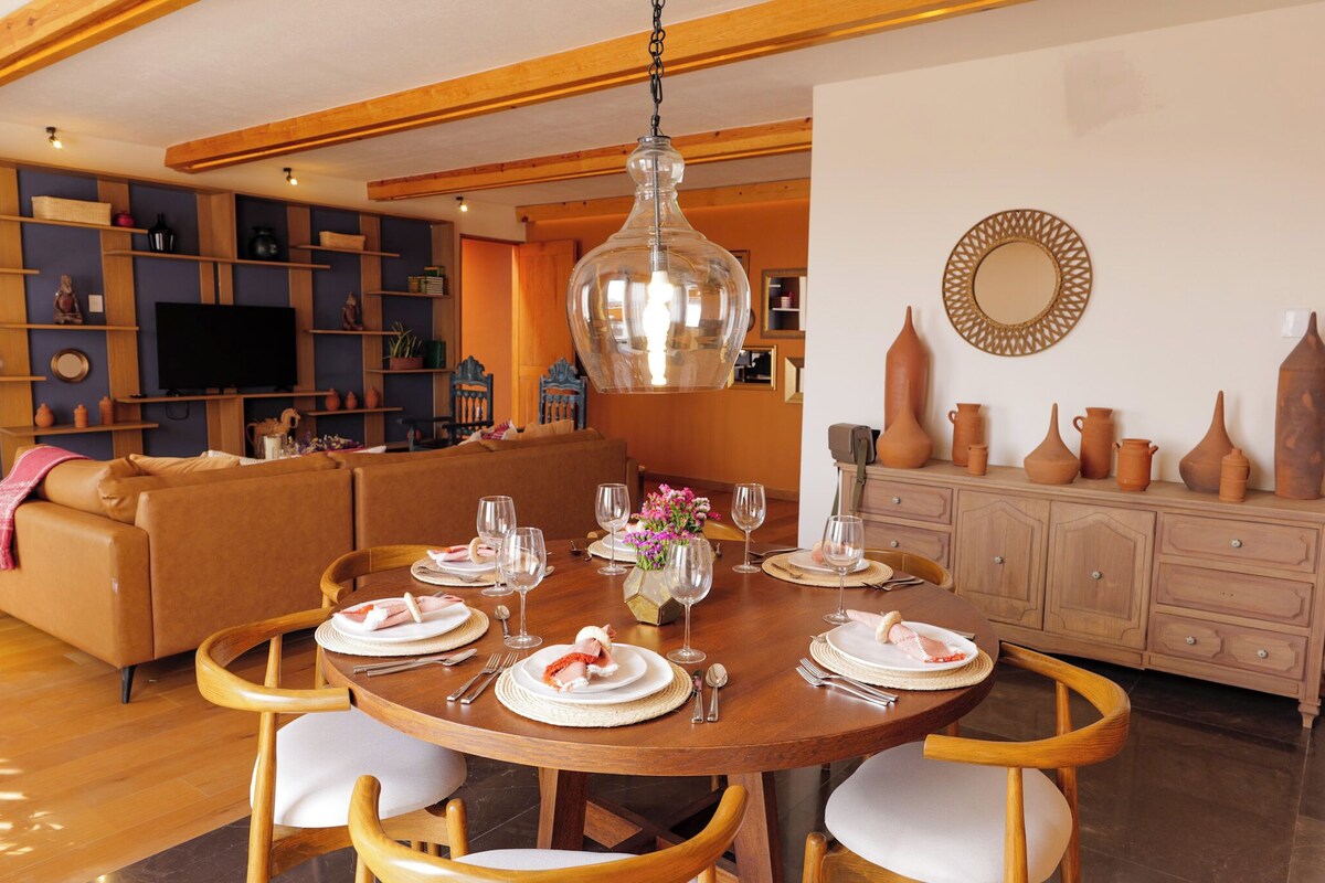 A dining area with a wooden table set for four, surrounded by wooden chairs.