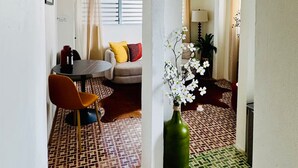 Una habitación con piso estampado, una mesa de comedor con sillas, un sofá con cojines y un jarrón verde con flores.