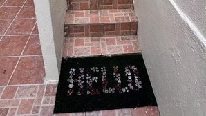 Un escalier en briques mène à une porte sur laquelle est posé un paillasson noir avec l’inscription « BIENVENUE ».