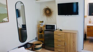Une chambre d’hôtel compacte comprenant un lit, une armoire en bois, un four à micro-ondes, une petite étagère avec quelques objets, une télévision et un miroir.
