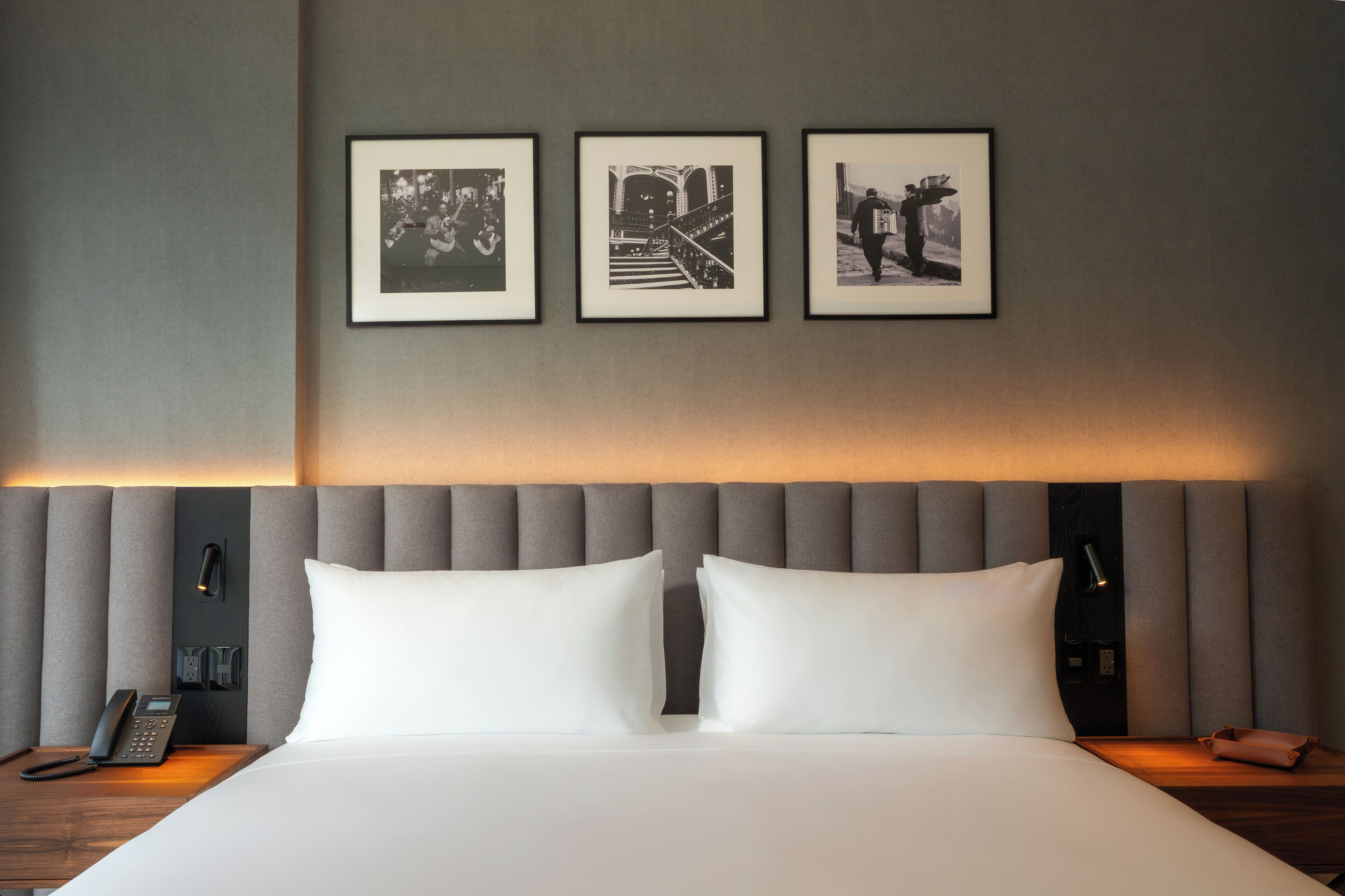 A hotel room with a bed, a nightstand, a phone, and three framed pictures on the wall.
