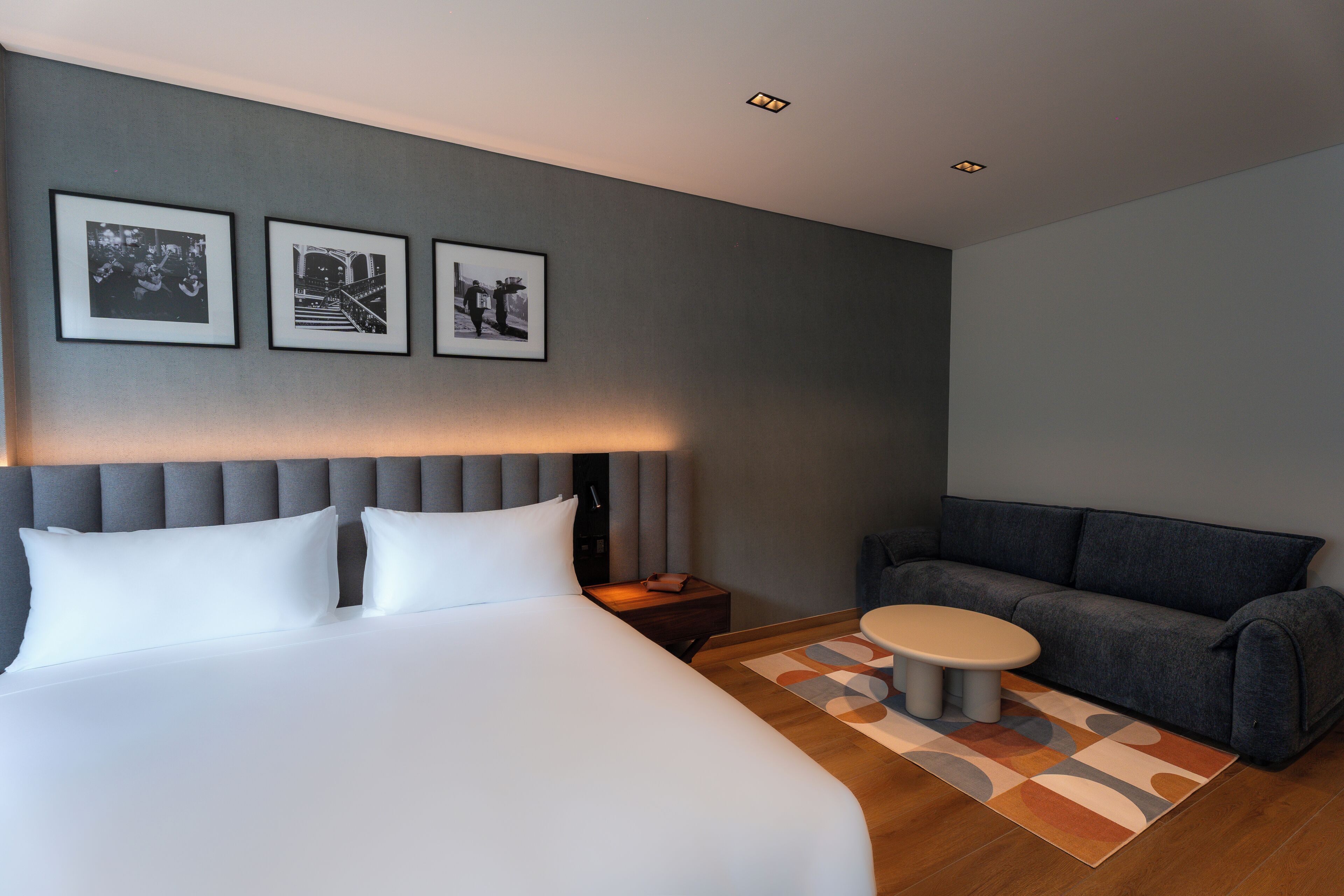 A hotel room with a large bed, a sofa, a small table, and three framed pictures on the wall.