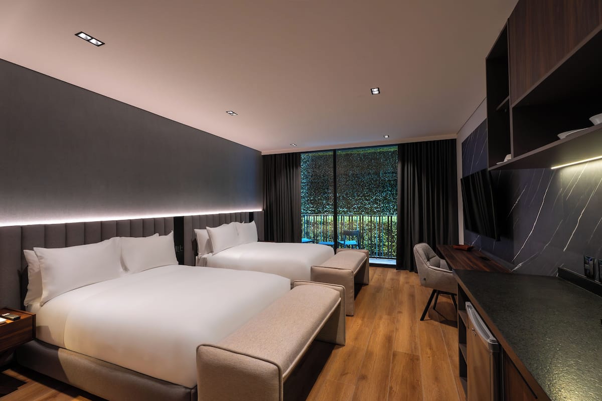 Una habitación de hotel moderna con dos camas, un escritorio y un televisor grande.