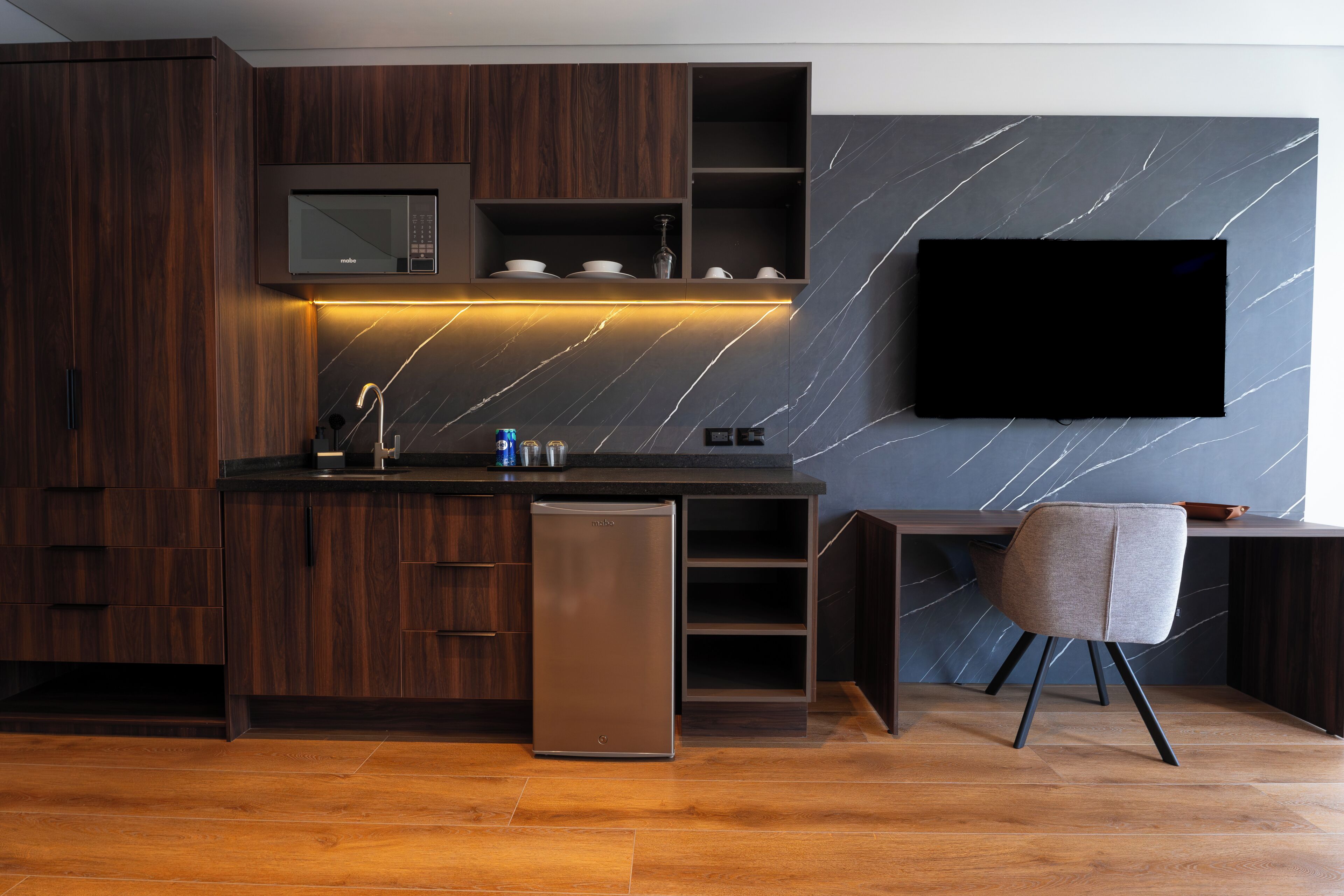 Une cuisine moderne avec des meubles en bois foncé, un four à micro-ondes encastré et un téléviseur à écran plat fixé à un mur en marbre.