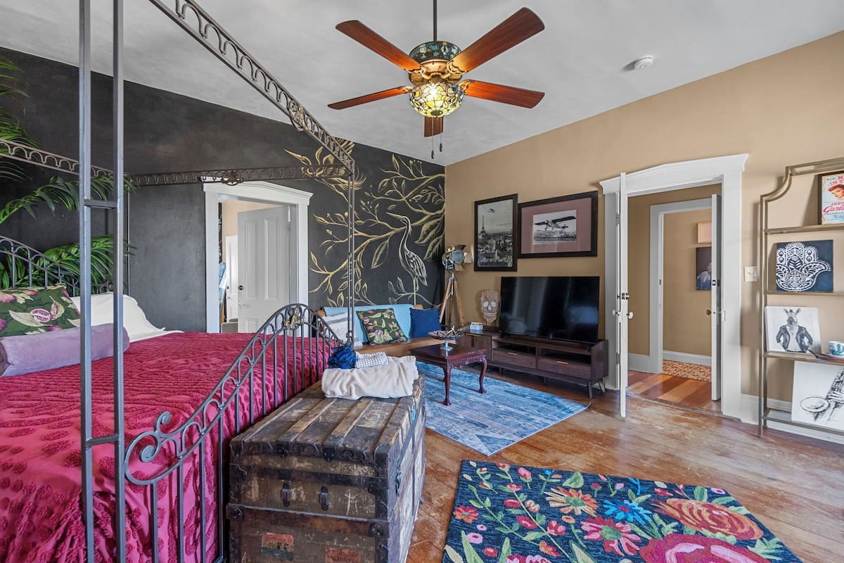 A bedroom with a bed, a chest of drawers, a dresser, a television, and a ceiling fan.