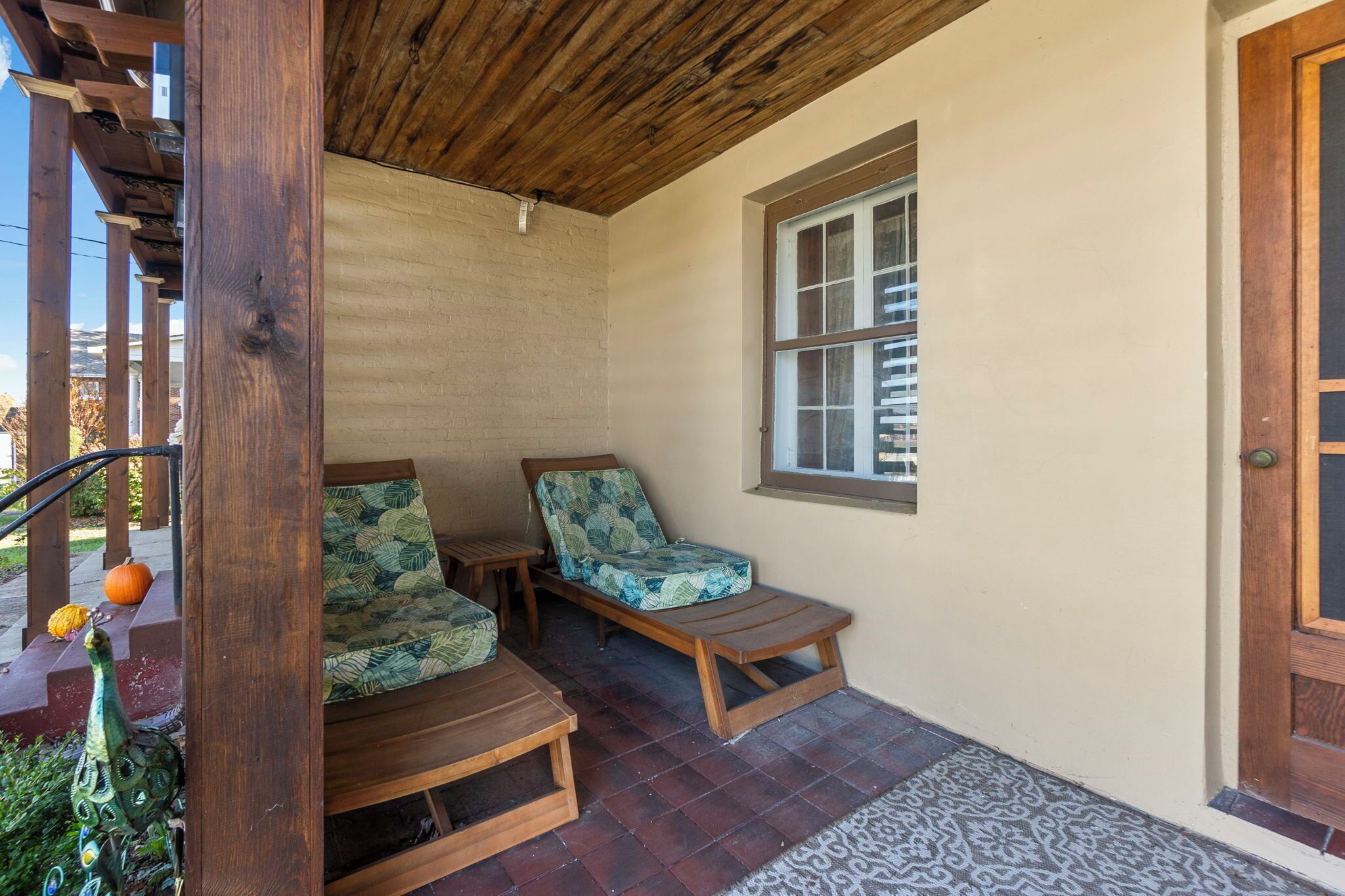 A covered porch with wooden furniture and a decorative peacock statue.