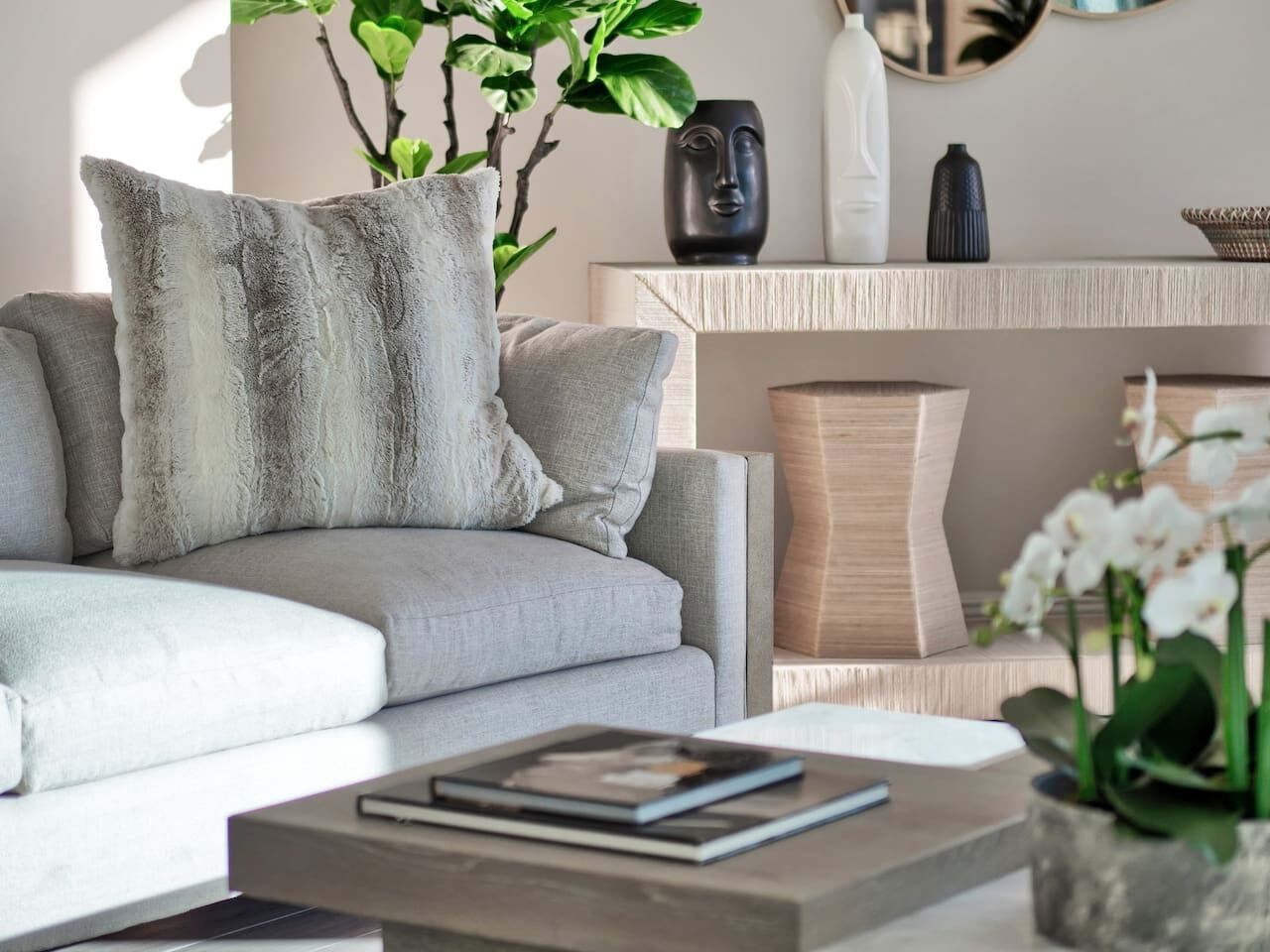 Een moderne woonkamer met een grijze bank, zachte kussens, een salontafel met een boek en een plant.